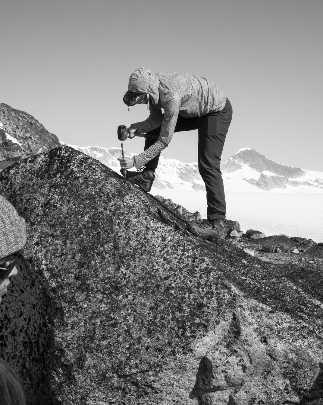 At a site called Taku D, above the Taku Glacier, Dibble uses a rubber mallet and a chisel to chip away flakes from the boulder to send to a lab for sampling.