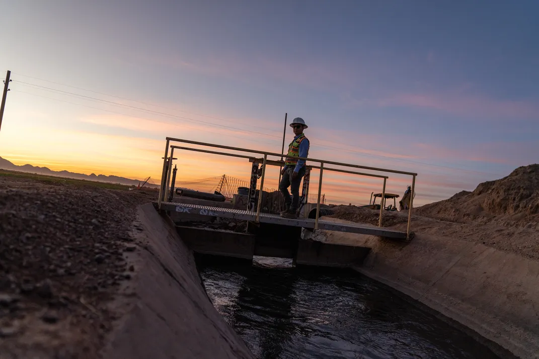 Downstream of a new pipeline that turns away from a major road, water is discharged into an open channel canal, which goes on to feed individual garden plots.